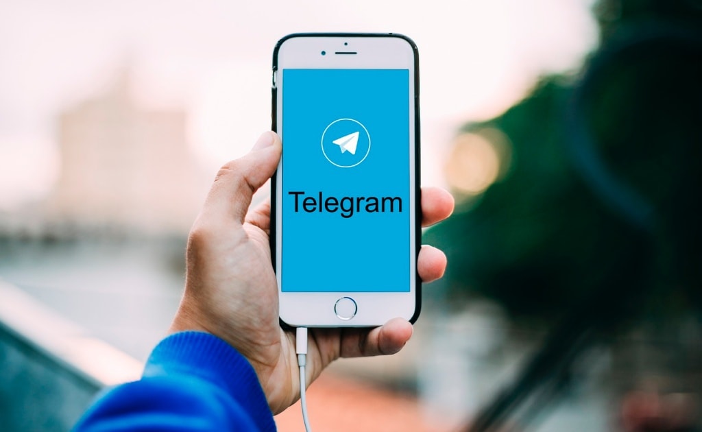 Person holding an iPhone with a black "Telegram" text and Telegram logo on-screen