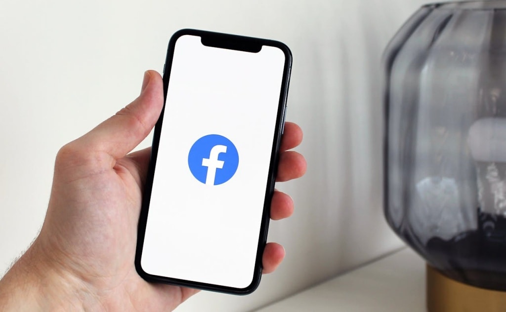 Person holding iPhone with Facebook logo on the screen